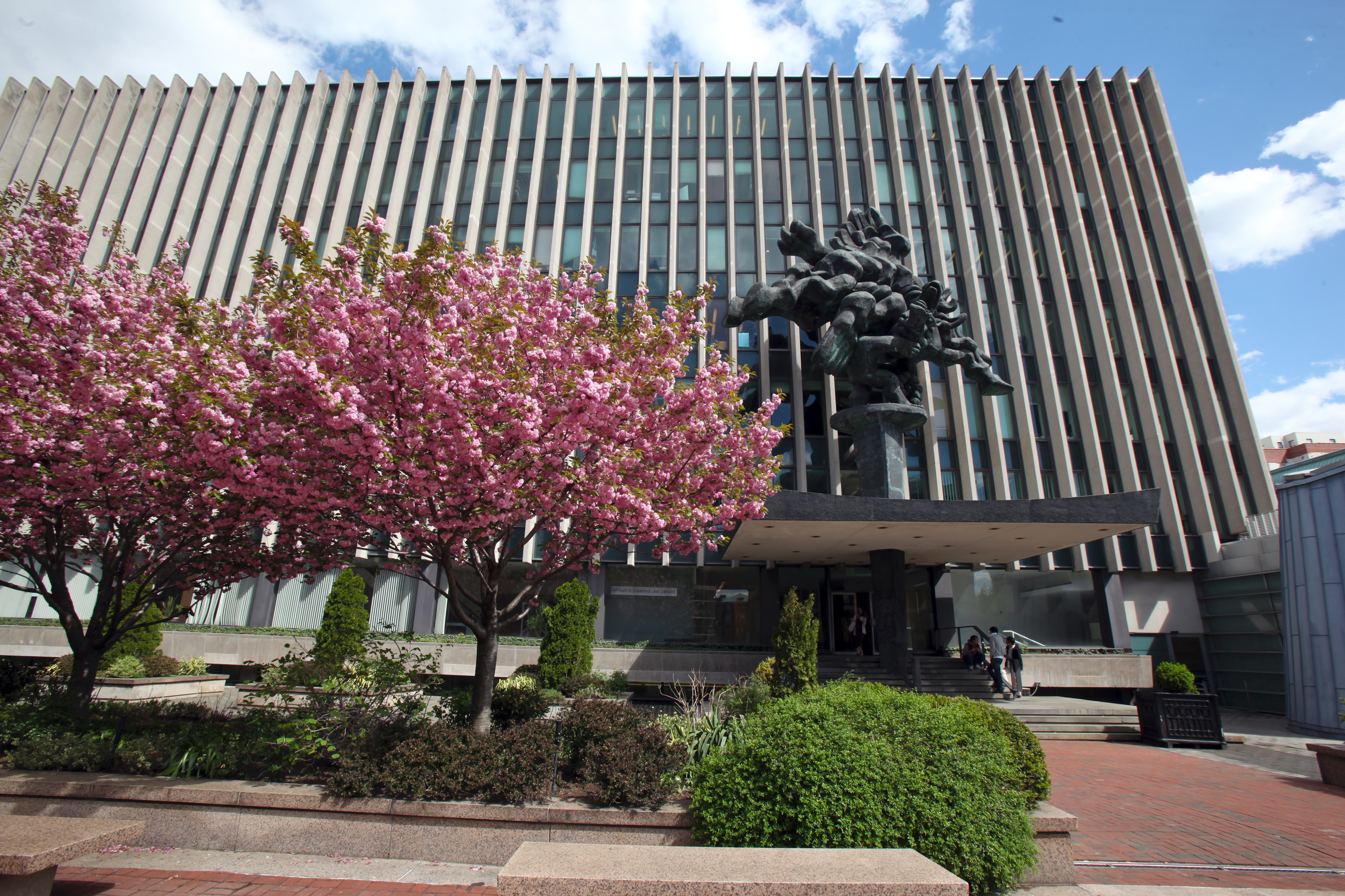 Columbia Law School, behind tress with cherry blossoms in full bloom, and an abstract statue