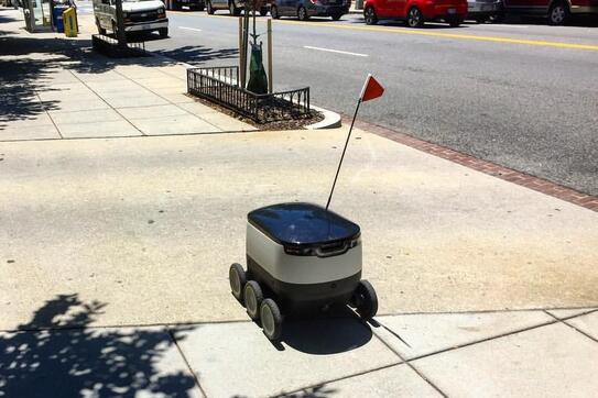 A robot on wheels and a flag on a sidewalk.