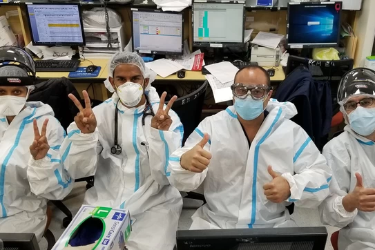 A group of healthcare workers wearing ppe throwing up peace signs and thumbs up.