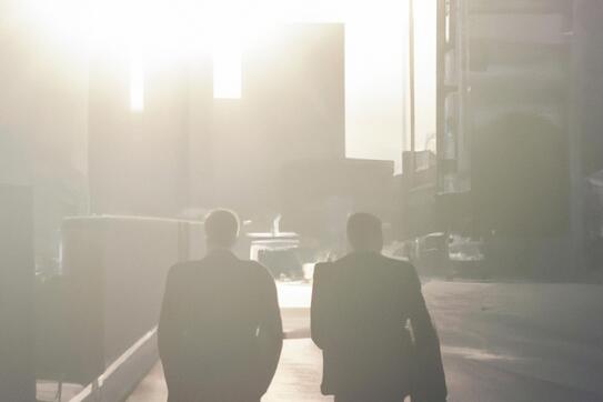 Two people in business suits walk away, toward tall buildings