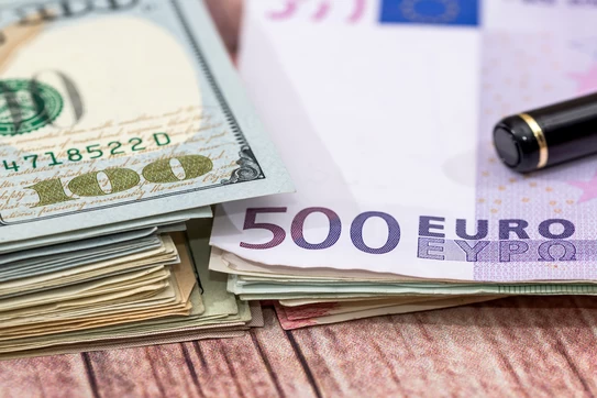Stacks of currency, US dollars, euros and a pen.