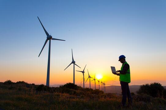An engineer working at a wind turbine farm at sunset.
