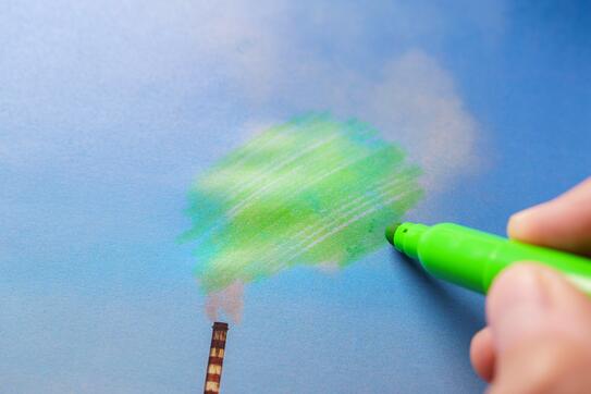 A hand holding a green marker, coloring in gray smoke that's pouring out of a smokestack