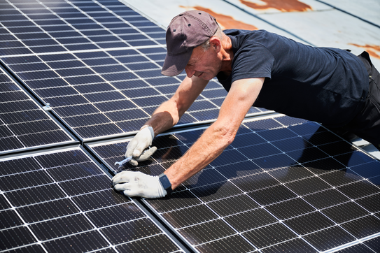 Worker building photovoltaic solar panel system on rooftop of house.