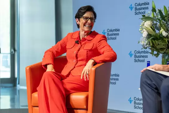 Jane Fraser, CEO of Citi, wearing an orange suit and sitting in an orange chair inside Cooperman Commons at Columbia Business School