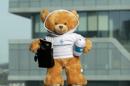 Marco, a small plush bear, wearing a CBS branded shirt and holding a CBS-branded notebook in one hand and a plush cup of coffee in the other