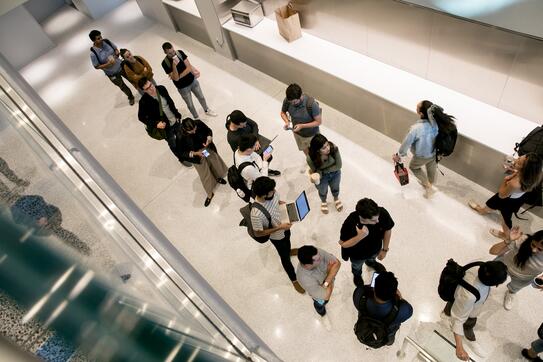 An overhead image of 10-15 students standing in Kravis Hall, speaking to each other