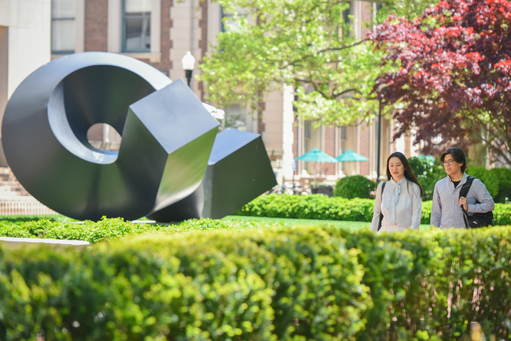 Two Asian students walk by The Curl sculpture on campus