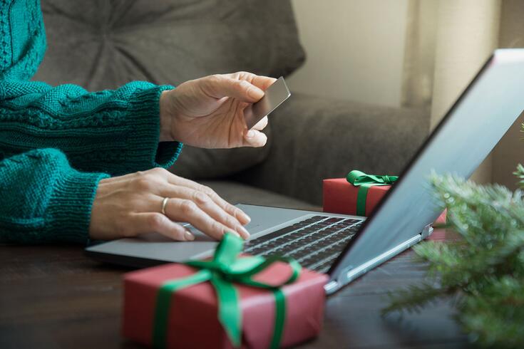 This stock photo features a woman shopping with a credit card and laptop at her home next to Christmas decorations