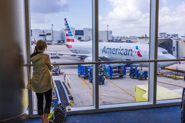 A woman looks out of an airport window at an airplane.