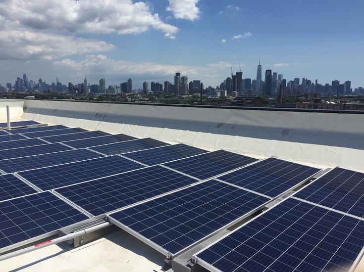 Solar panels on a rooftop with the New York City skyline in the background.