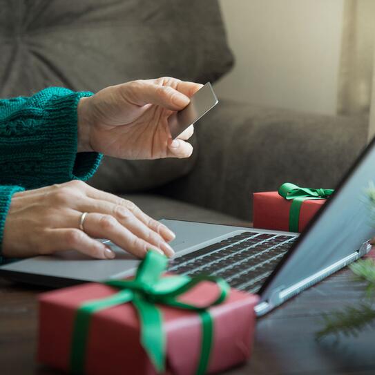 This stock photo features a woman shopping with a credit card and laptop at her home next to Christmas decorations